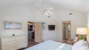 Ein Schlafzimmer mit einem Bett, einem Schminktisch, einem Deckenventilator, einem Fernseher und einer Tür, die auf einen Balkon führt.