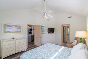 A bedroom with a bed, a dresser, a ceiling fan, a TV, and a door leading to a balcony. - Sun Realty pet-friendly oceanside Duck home with hot tub (Duck)