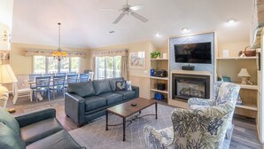 Ein Wohnzimmer mit Sofa, Sessel, Couchtisch, Kamin, Fernseher und Essbereich mit Stühlen und Tisch.