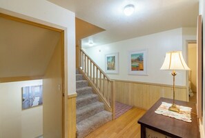 A staircase leading to a second floor, a wooden floor, a wall with framed artwork, and a table with a lamp. - Sun Realty pet-friendly oceanside Duck home with hot tub (Duck)