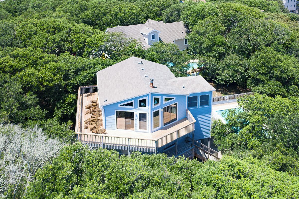 A two-story house with a large deck, surrounded by dense greenery.