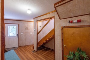 A hallway with a wooden staircase, a door with a window, and a fire extinguisher on the wall. - Sun Realty pet-friendly oceanside home with private pool! (Duck)