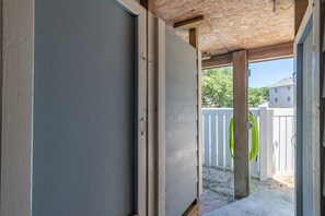 An open door leading to a covered outdoor area with a wooden ceiling and a white fence in the background. - Sun Realty pet-friendly oceanside home with private pool! (Duck)