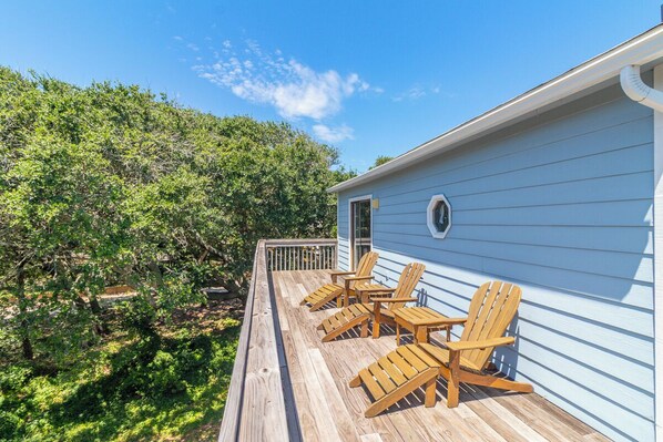 A wooden deck with outdoor furniture, a blue building, and a lush green landscape. - Sun Realty pet-friendly oceanside home with private pool! (Duck)