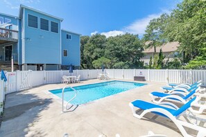 A swimming pool with lounge chairs, a small table, and a white fence. - Sun Realty pet-friendly oceanside home with private pool! (Duck)