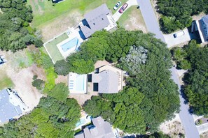 An aerial view of a residential area with a house surrounded by trees, a swimming pool, and a road. - Sun Realty pet-friendly oceanside home with private pool! (Duck)