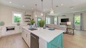 A modern kitchen with a central island, white cabinetry, and pendant lighting. - dreAMI - Luxury Island Home - Anna Maria - By Island Real Estate (Holmes Beach)
