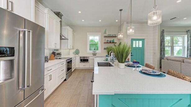 A modern kitchen with white cabinetry, a large island, stainless steel appliances, and pendant lighting. - dreAMI - Luxury Island Home - Anna Maria - By Island Real Estate (Holmes Beach)