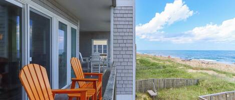 A beachfront property with a balcony, outdoor seating, and a view of the beach.