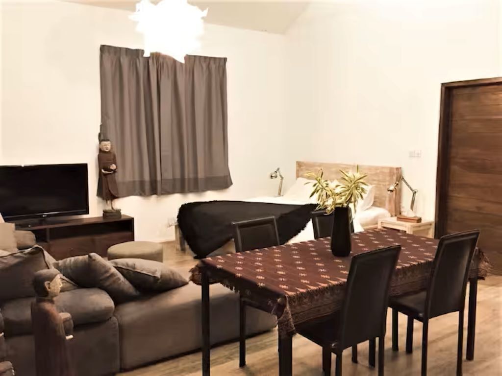 A living room with a sofa, a TV, a dining table with chairs, and a bed with a headboard.