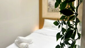Ein Hotelzimmer mit einem ordentlich bezogenen Bett, einem weißen Kopfkissen und einer an der Wand hängenden Pflanze.