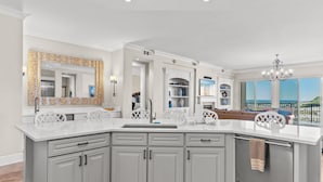 A modern kitchen with a large island, white cabinetry, and a view of the ocean. - 5 Bedroom • 4.5 Bath • Sleeps 10 • Gulf-Front • Includes 1 Complimentary Beach S (Santa Rosa Beach)