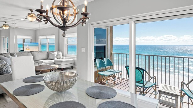 A spacious living area with a large window overlooking the ocean, a chandelier, and a balcony with wicker furniture. - Gulf Front Condo in Gated Crystal Beach Complex, End Unit (Destin)