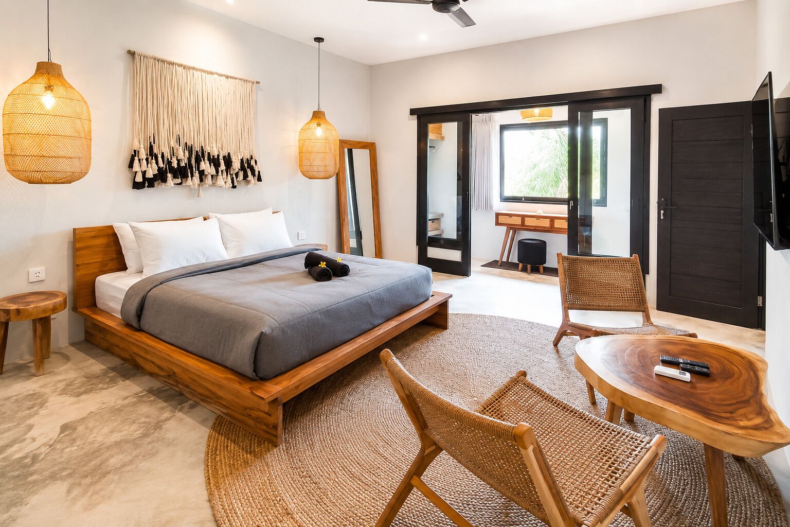 A modern bedroom with a wooden bed, a round wooden table, wicker chairs, and a large window.