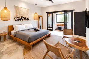 Ein modernes Schlafzimmer mit einem hölzernen Bett, einem runden Holztisch, Korbstühlen und einem großen Fenster.