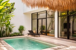 Ein moderner Poolbereich mit einer gläsernen Lounge, tropischen Pflanzen und einem Reetdach.