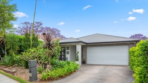 A residential house with a garage, surrounded by lush greenery and a clear blue sky. - Bright Family Home in Rydalmere With Yard & BBQ (Sydney)