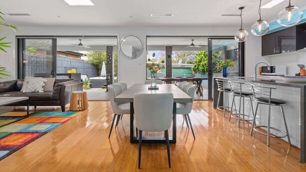 A modern kitchen with a central island, bar stools, and a dining area with a table and chairs. - Bright Family Home in Rydalmere With Yard & BBQ (Sydney)