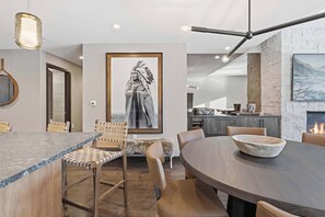 A modern dining area with a round table, chairs, a large framed artwork, and a stone fireplace. - The Lion Residences W201 (Vail)