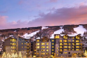 A multi-story hotel with a stone facade, multiple balconies, and a view of a snowy mountain. - The Lion Residences W201 (Vail)
