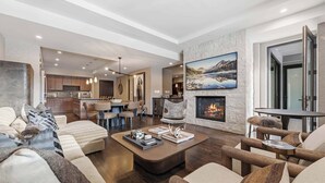 A spacious living area with a fireplace, modern furniture, and a view of the kitchen. - The Lion Residences W201 (Vail)