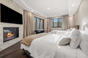 A modern bedroom with a fireplace, a large bed, and a TV mounted on the wall. - The Lion Residences W201 (Vail)