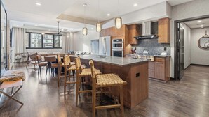 A modern kitchen with wooden cabinets, a central island with bar stools, and a large window providing natural light. - The Lion Residences W201 (Vail)