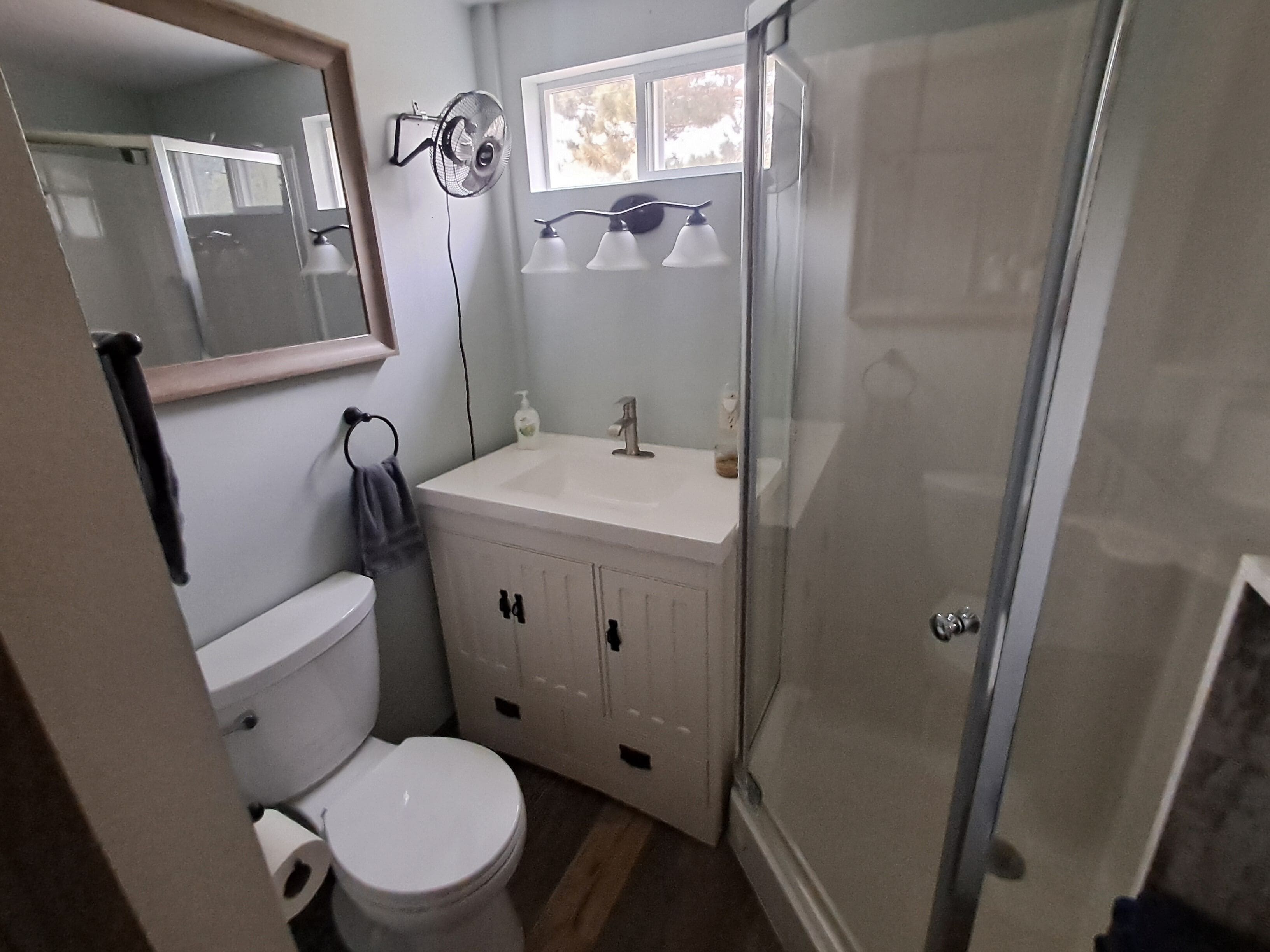 Et badeværelse med toilet, vask, spejl og bruser.