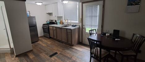 A compact kitchen with a dining area, wooden flooring, and a ceiling fan.