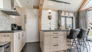 Ett modernt kök med ljusa träskåp, en svart bänkskiva och en inbyggd spis. Det finns två barstolar och ett fönster med gardiner.