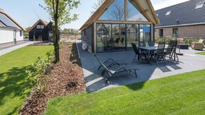 Ett modernt hus med ett stort glashus, en uteplats med utemöbler och en välskött trädgård.