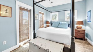 Een kamer met een hemelbed, blauwe wanden, een plafondventilator en een raam met jaloezieën.