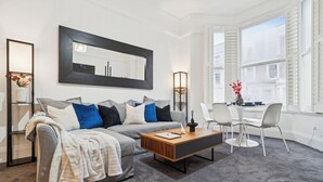 Ein modernes Wohnzimmer mit einem grauen Sofa, einem Holztisch und einem Essbereich mit weißen Stühlen.