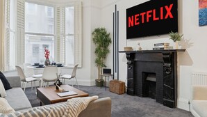 Ein Wohnzimmer mit Kamin, einem an der Wand befestigten Fernseher und einem Essbereich mit Stühlen und Tisch.