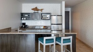 Une cuisine moderne avec un îlot central, des tabourets de bar, un four à micro-ondes, un réfrigérateur et un motif décoratif représentant des poissons sur le mur.