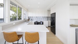 A modern kitchen with white cabinetry, a large island with two chairs, and a black refrigerator. - Spacious 5-bed Beach House With Ocean View (Sydney)