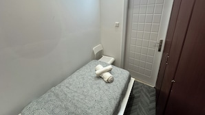 Um quarto pequeno e estreito com uma cama de solteiro, uma porta branca e um guarda-roupa de madeira.
