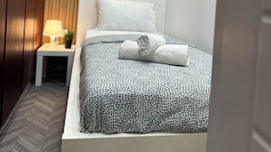 Uma cama bem arrumada com colcha estampada, uma mesa de cabeceira com abajur e um painel com um letreiro emoldurado.
