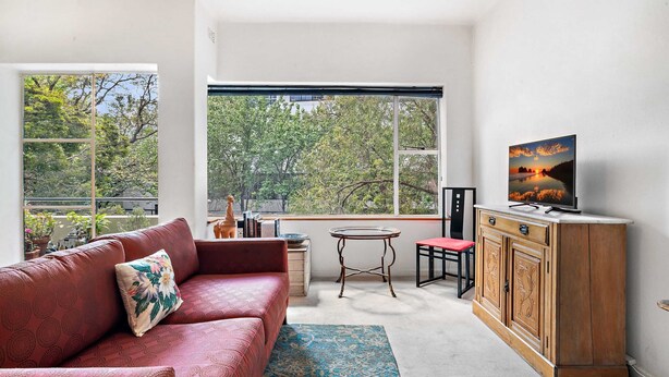Una sala de estar con un sofá rojo, una mesita, un mueble aparador y un televisor sobre un pedestal.