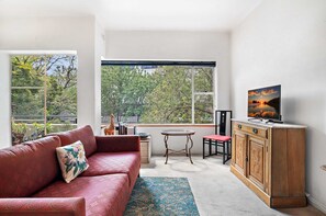 A living room with a red sofa, a small table, a cabinet, and a TV on a stand. - Sunny 1-bed With Parking Near Arts Precinct (Melbourne)