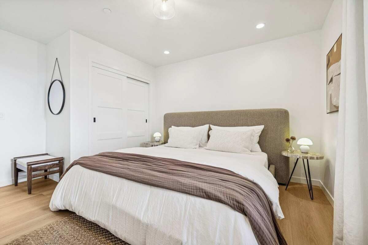 A bedroom with a large bed, a bedside table with a lamp, a small side table, and a door.