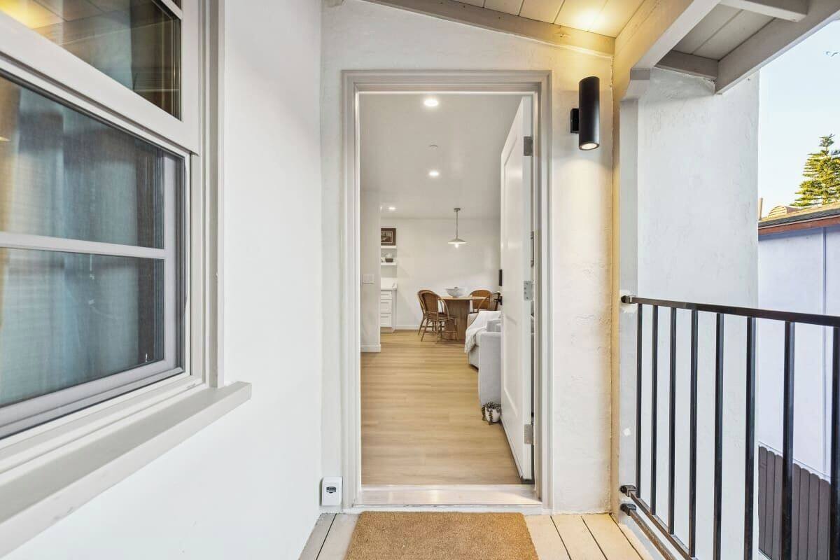 Un couloir menant à une salle à manger dotée d’un plancher en bois, de murs blancs et d’une rambarde noire.