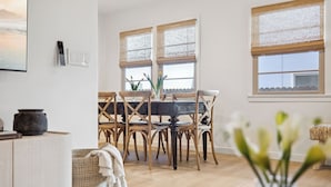 Ein Essbereich mit einem Holztisch und Stühlen, einer Blumenvase und Blick ins Freie durch die Fenster.