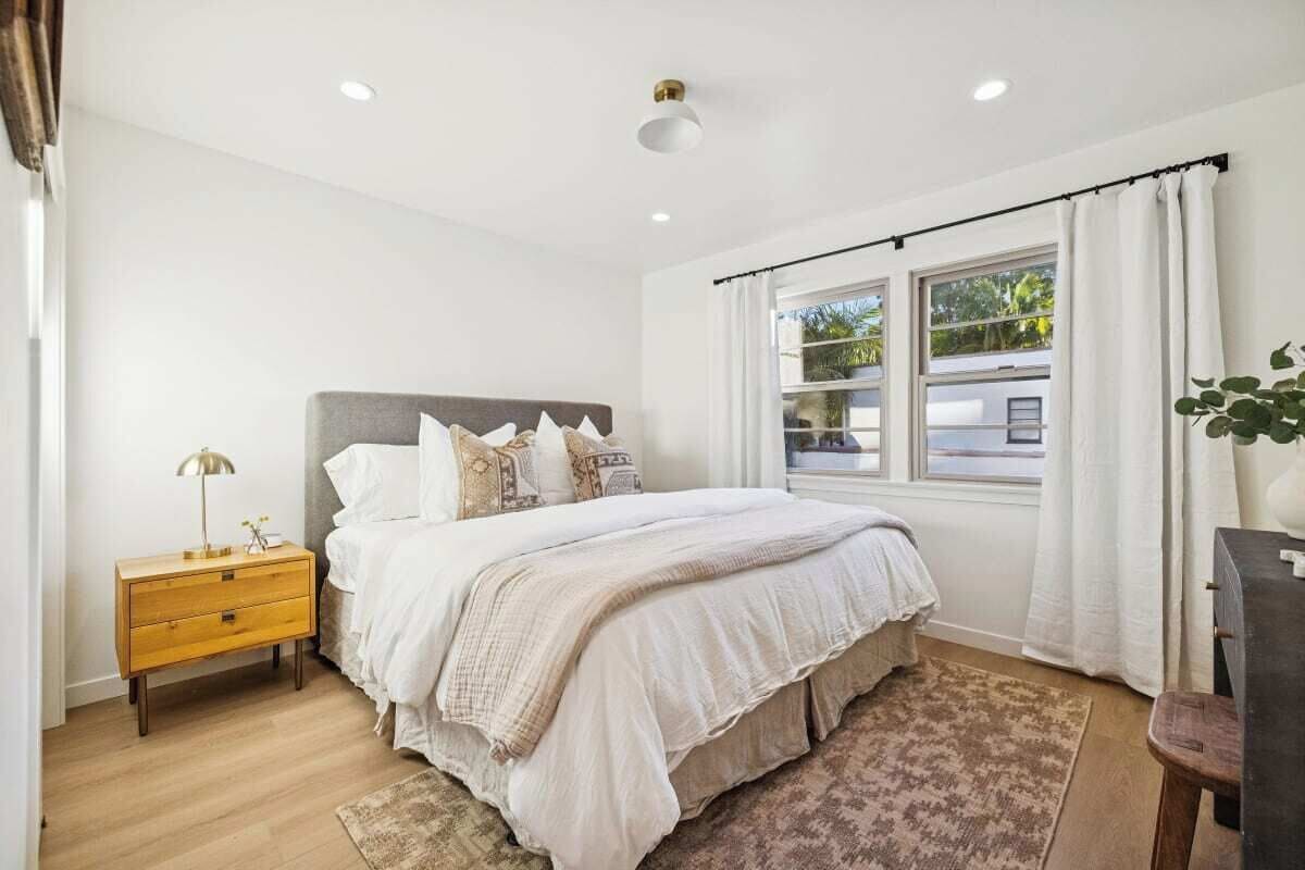 A bedroom with a bed, bedside table, and a window with curtains.