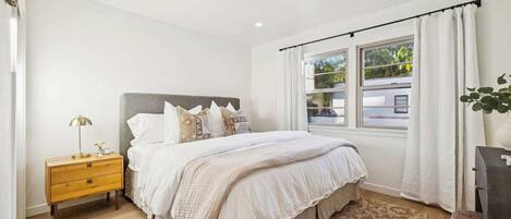 A bedroom with a bed, bedside table, and a window with curtains.