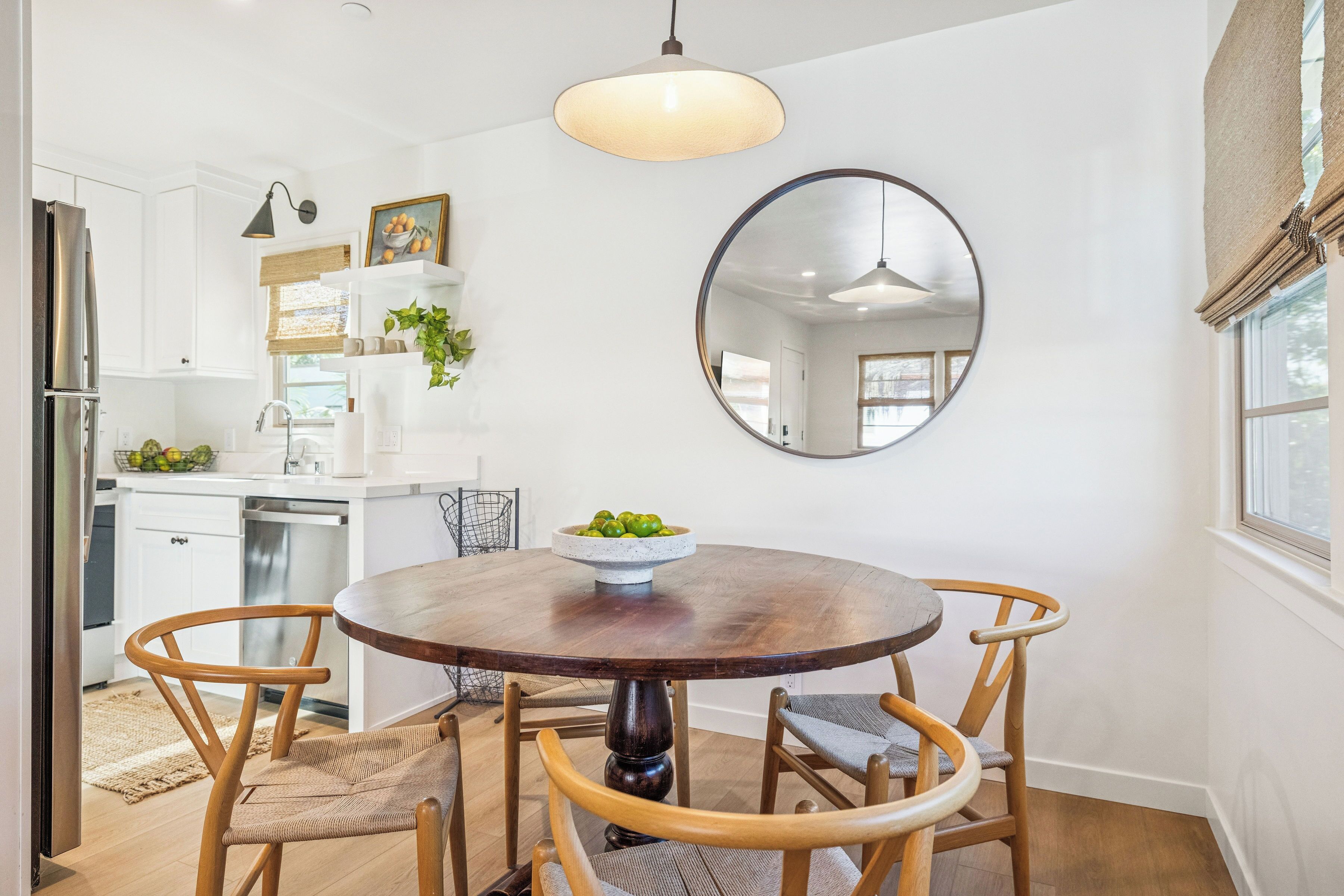 A modern kitchen with white cabinets, a wooden dining table, and a round mirror.