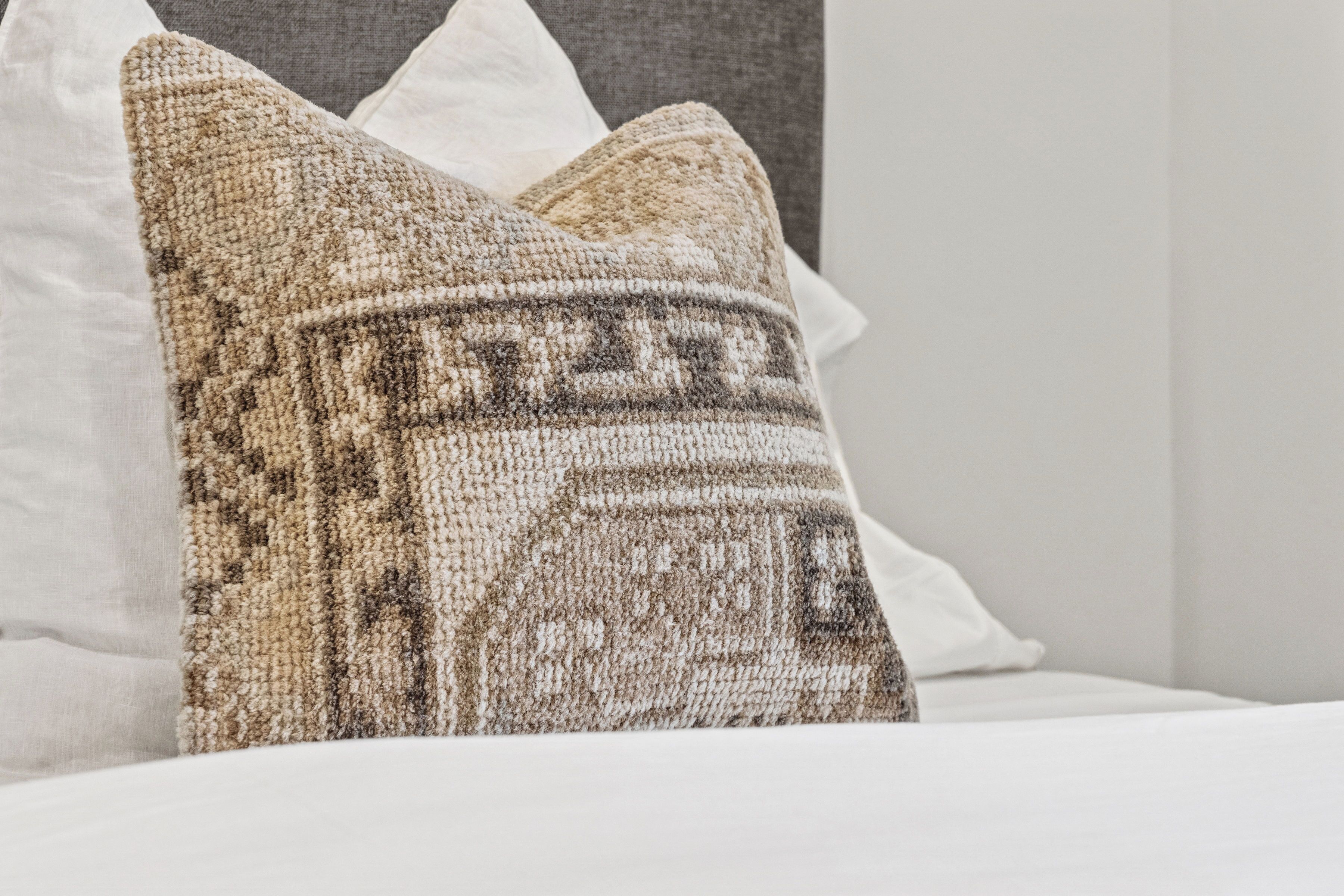 Ein Bett mit weißer Bettwäsche und einem Kissen mit Muster.