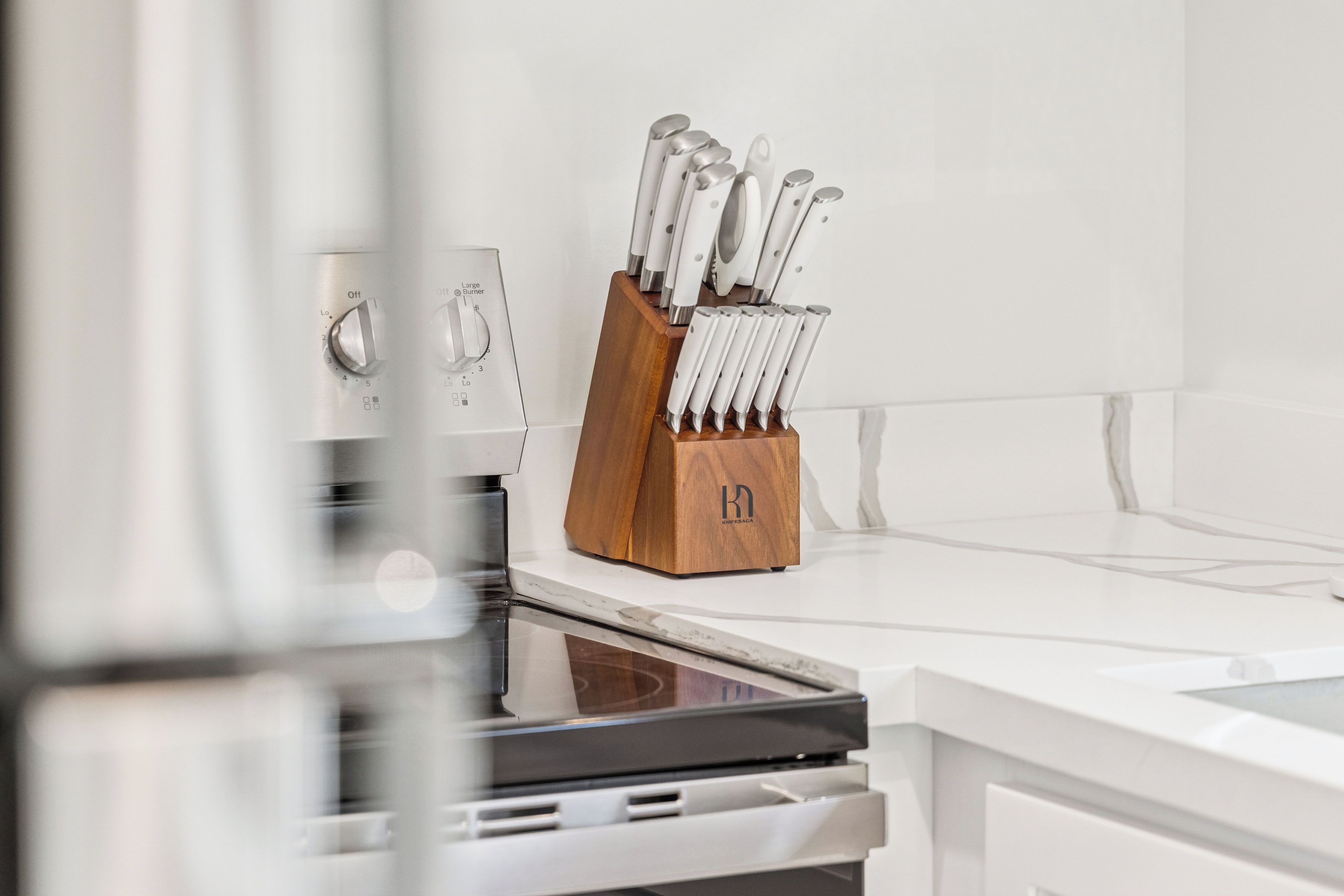 A kitchen with a white countertop, a wooden knife block, and a stainless steel oven.
