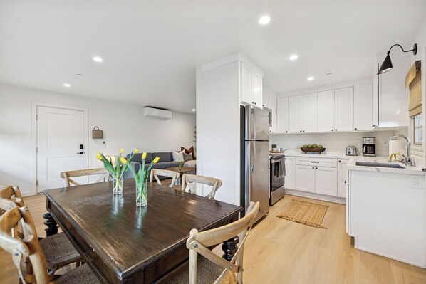 A modern kitchen with white cabinets, a wooden dining table, and a built-in refrigerator. - Casa Yano by The Beach (Santa Barbara)