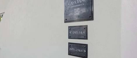 Un mur sur lequel sont affichées trois plaques indiquant les numéros des chambres : « CASA YANO SANTA BARBARA CA », « UNITÉS 3 ET 4 » et « UNITÉS 1, 2, 5 ET 6 ».
